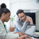 Software engineers collaborating during coding practice, with a mentor guiding and reviewing code on computer screens.