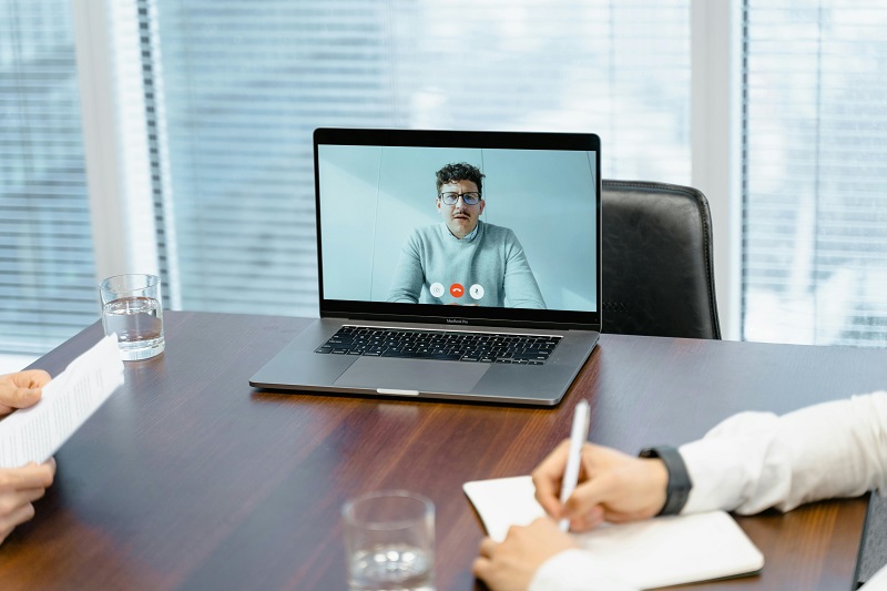 Excited developer in video interview on laptop during virtual tech job discussion, surrounded by notes and water glass on wooden desk.